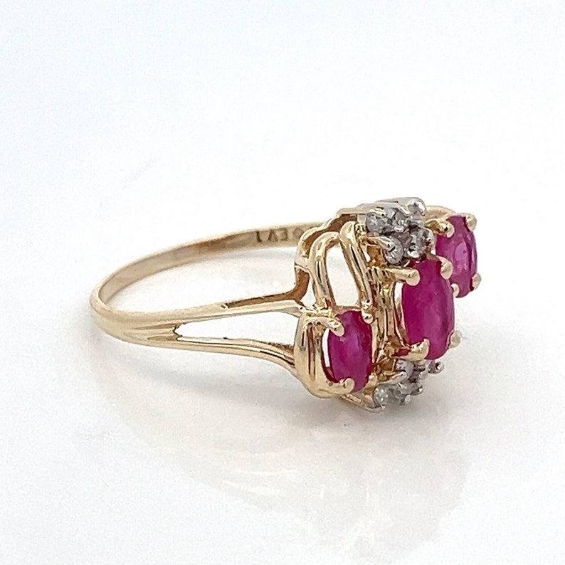 May include: A gold ring featuring three oval-shaped ruby stones and smaller diamonds set in a delicate, interwoven design.