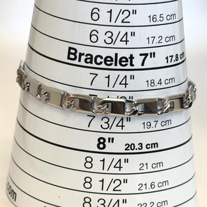 May include: A silver bracelet with rectangular links is displayed on a bracelet sizing cone. The cone shows measurements in inches and centimeters, with the bracelet appearing to be approximately 7 inches (17.8 cm) in length.