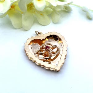 May include: A gold heart-shaped locket with a detailed design. The locket has a hinged opening and features a ruby-colored stone in the center of two interlocking hearts.