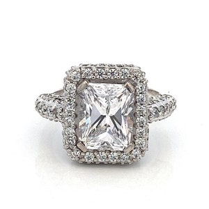 May include: A silver ring with a large, clear, square-shaped diamond set in a double halo of smaller diamonds.