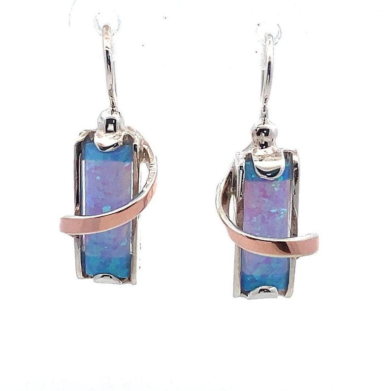 May include: A pair of silver earrings with a pink and blue opal stone set in a silver and rose gold swirl design.