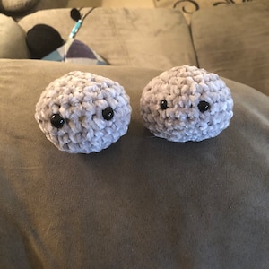 May include: Two gray crocheted plush toys with black button eyes. The toys are round and have a fuzzy texture.