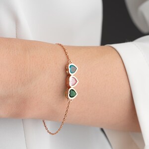 May include: A delicate rose gold bracelet with three heart-shaped gemstones in teal, pink, and green. The bracelet has a chain-link design. The gemstones are set in a bezel setting. Ideal for adding a touch of colour to any outfit.