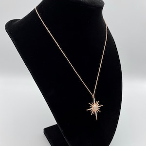 May include: A rose gold necklace featuring a starburst pendant. The pendant is made of silver and has small clear stones set into it.