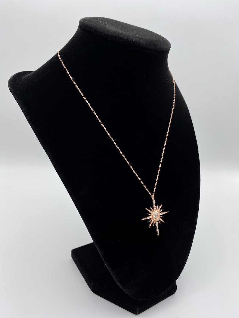 May include: A rose gold necklace featuring a starburst pendant. The pendant is made of silver and has small clear stones set into it.