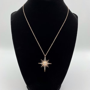 May include: A rose gold necklace featuring a starburst pendant set with clear cubic zirconia stones.
