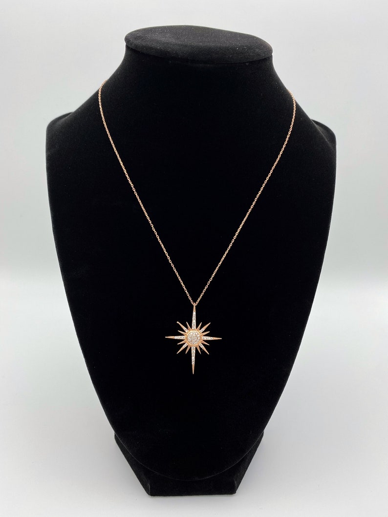 May include: A rose gold necklace featuring a starburst pendant set with clear cubic zirconia stones.