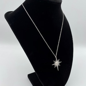 May include: A silver chain necklace with a starburst pendant. The pendant is made of silver and has a clear crystal centre.