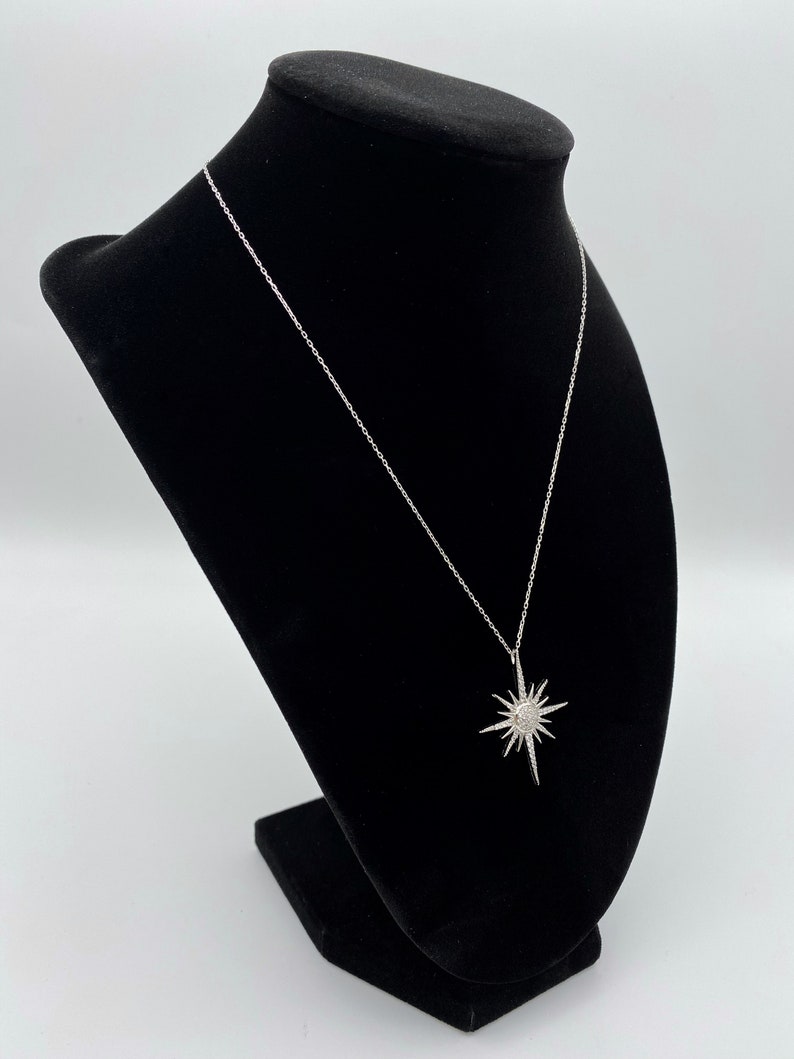May include: A silver chain necklace with a starburst pendant. The pendant is made of silver and has a clear crystal centre.