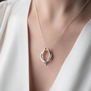 Puede incluir: Un collar de plata con un colgante geométrico. El colgante está hecho de dos círculos entrelazados, creando un diseño único y moderno.