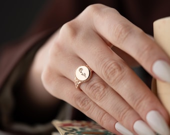 Puede incluir: Un anillo de oro con un diseño de rosa en la parte superior. El anillo está en el dedo de una persona.