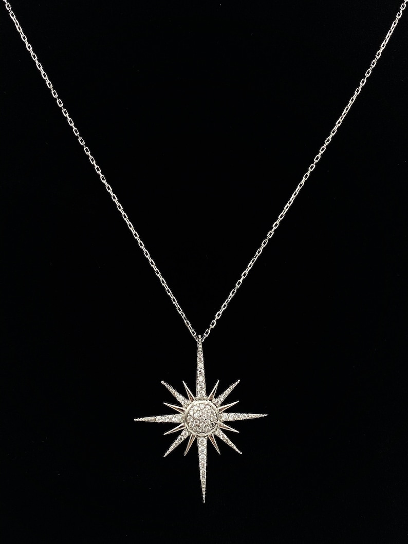 May include: A silver necklace featuring a starburst pendant set with clear cubic zirconia stones.