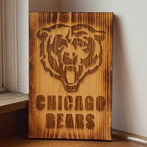 Puede incluir: Un letrero de madera con un acabado quemado presenta una imagen tallada de la cabeza de un oso con el texto "CHICAGO BEARS" debajo.