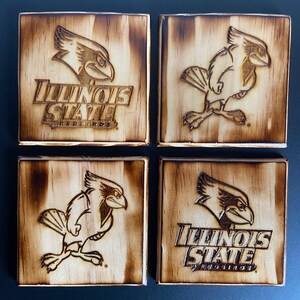 May include: Set of four wooden coasters featuring a burnt-in design of the Illinois State Redbirds logo. Each coaster has a different design, with some featuring the mascot and others featuring the team name.
