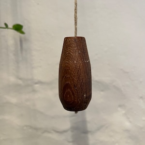 May include: A dark brown wooden light pull with a natural grain pattern. The pull is attached to a string.