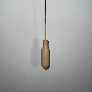 May include: A wooden light pull with a natural finish. The pull is attached to a silver cord.