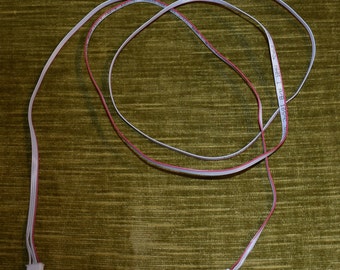 May include: A white cable with red wires running through it. The cable has two white connectors on the ends. The cable is coiled up on a green surface.