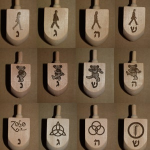 May include: A collection of twelve wooden dreidels. Each dreidel features a unique design, including walking figures, dancing bears, and symbols. The designs are etched into the light-colored wood, with Hebrew letters on the bottom.
