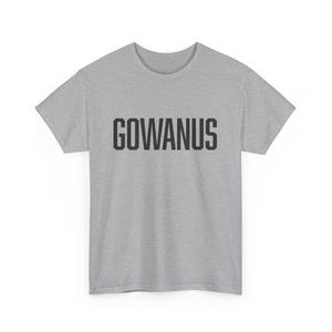 以下が含まれることがあります： 胸に太字の黒い大文字で「GOWANUS」とプリントされた、ヘザーグレーのTシャツ。Tシャツは半袖で、クルーネックです。