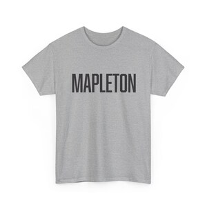 May include: A heather gray t-shirt with the word "MAPLETON" printed in bold, black capital letters across the chest. The shirt has short sleeves and a crew neck.