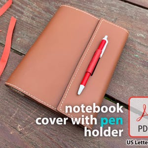 May include: A brown leather notebook cover with a pen holder and a red pen. The cover is closed and has white stitching around the edges. The text "notebook cover with pen holder" is visible. A red ribbon is on the left.