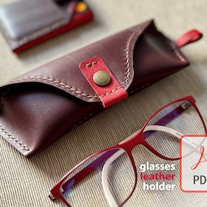 May include: A burgundy leather glasses case with a red leather flap and a brass button closure. The case is lying on a beige fabric surface next to a pair of red-rimmed glasses. The text "glasses leather holder PDF" is visible in the lower right corner of the image.