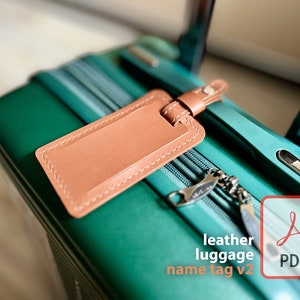 May include: A brown leather luggage tag with stitching around the edges attached to a teal suitcase.