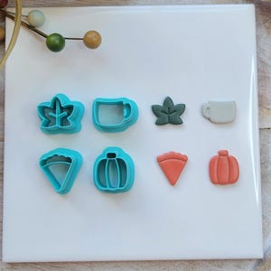 May include: A collection of fall-themed cookie cutters in various shapes, including a maple leaf, coffee mug, pumpkin, and pie slice. The cutters are in shades of teal, green, and orange, perfect for autumn baking.
