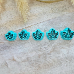 May include: Five teal blue plastic leaf-shaped cookie cutters on a light wood surface.