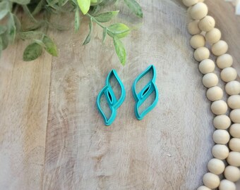 May include: Two turquoise leaf-shaped cookie cutters on a wooden surface.