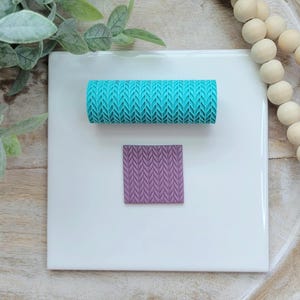 May include: A teal blue and purple silicone rolling pin and stamp with a knit pattern. The rolling pin and stamp are on a white surface.