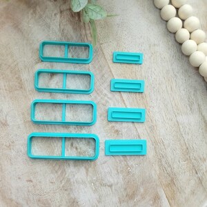 May include: Set of six turquoise plastic cookie cutters in various sizes, shaped like rectangles with a horizontal line in the middle.