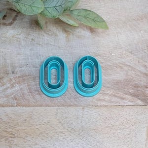 May include: Two teal blue plastic cookie cutters shaped like the number zero. The cutters are nested inside each other.