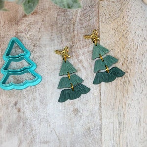 May include: A pair of green and gold Christmas tree earrings. The earrings are made of layered felt and have a gold hook closure.