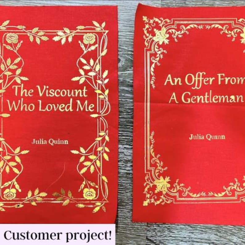 May include: Two red fabric book covers with gold lettering and ornate gold borders. The covers are for the books "The Viscount Who Loved Me" and "An Offer From A Gentleman" by Julia Quinn.