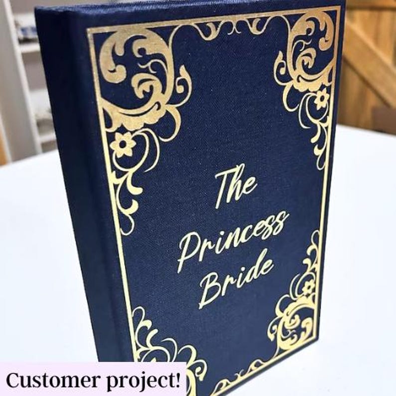 May include: A navy blue book with gold lettering and decorative accents. The title of the book is "The Princess Bride".