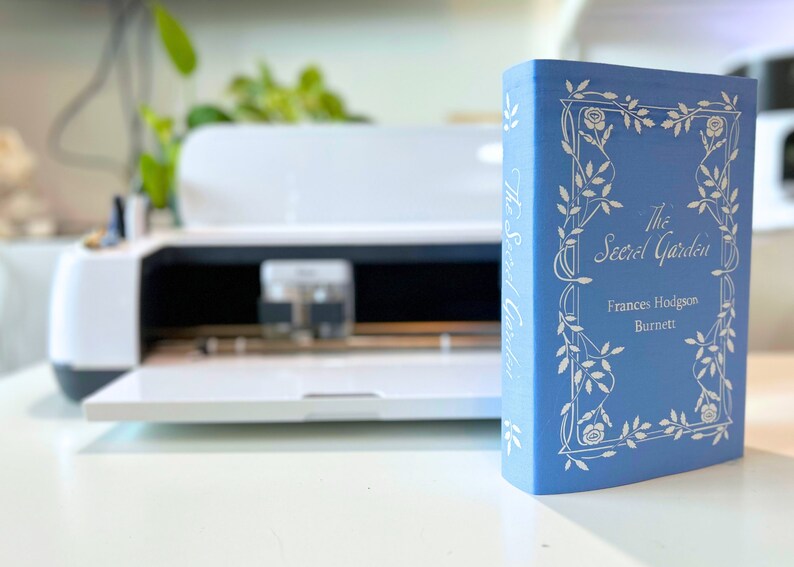 May include: A blue hardcover book titled "The Secret Garden" by Frances Hodgson Burnett. The book cover features a white floral design.