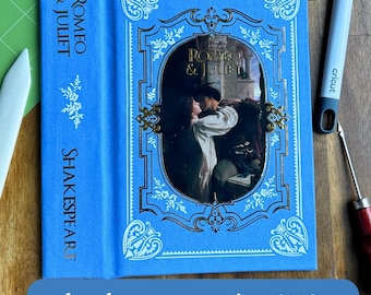 Puede incluir: Una cubierta de libro azul con un diseño dorado y blanco. El título "Romeo y Julieta" está impreso en dorado en la cubierta. El lomo del libro también es azul y tiene el nombre del autor "Shakespeare" impreso en dorado.