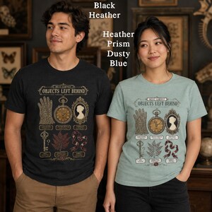 May include: Two short-sleeve crew neck t-shirts in black heather and heather prism dusty blue. Each shirt features a graphic print titled Relic Cabinet Objects Left Behind, displaying illustrations of a lace glove, pocket watch, portrait, key, fern, and ribbon.