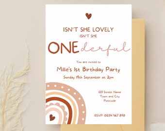 May include: A pink and brown illustrated rainbow with white polka dots and a heart at the bottom. The text "ISN'T SHE LOVELY ISN'T SHE ONEderful" is at the top of the card. The text "You are invited to Millie's 1st Birthday Party Sunday 19th September at 2pm 123 Street Name Town and City Postcode RSVP: 01234 567 890" is below the rainbow.