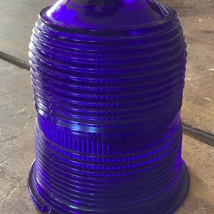 May include: A deep blue, vintage-style glass object with a rounded top and a ridged, cylindrical body. The glass has a glossy finish and appears to be a decorative piece or a lamp shade. The object sits on a flat base.