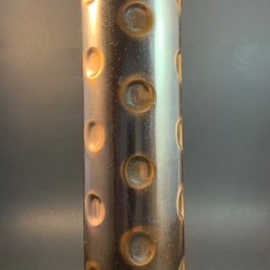 May include: A tall, cylindrical vase with a copper-colored finish and a textured surface. The vase has a pattern of raised circles around its entire surface.