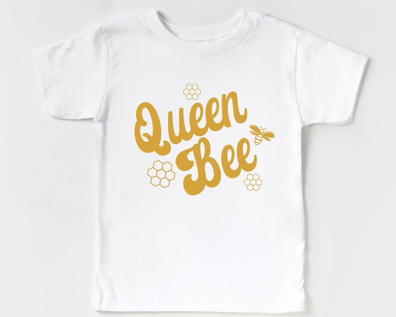 May include: White t-shirt with a gold graphic that says "Queen Bee" with a bee and honeycomb designs.
