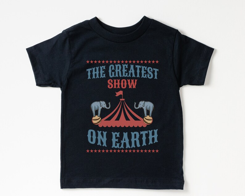 May include: A black t-shirt with a white and red circus tent graphic and the text "The Greatest Show On Earth" printed on it.