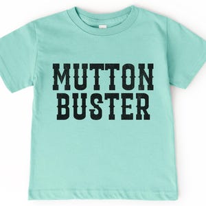 May include: A light blue t-shirt with the text "MUTTON BUSTER" printed in black.