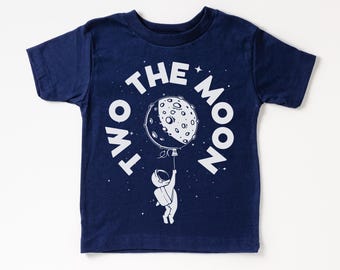 May include: A navy blue t-shirt with a white graphic of an astronaut holding a moon balloon. The text "To the Moon" is written in a circle around the astronaut.