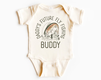 May include: A cream-colored baby onesie with a graphic of a trout jumping out of the water. The text "Daddy's Future Fly Fishing Buddy" is printed in a circle around the fish.