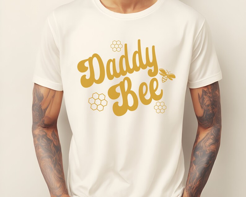 May include: White t-shirt with a gold graphic that says "Daddy Bee" with a stylized bee illustration.