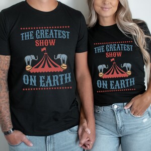 May include: A matching set of black t-shirts with a circus theme. The shirts feature a red and white striped tent with two elephants balancing on balls. The text on the shirts reads "The Greatest Show On Earth".