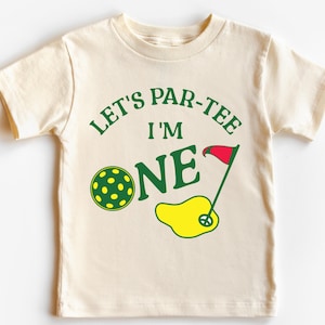 May include: A white t-shirt with green text that says "Let's Par-Tee I'm One" with a green golf ball and a red golf flag.